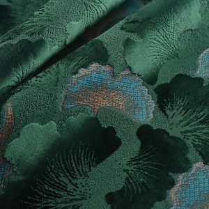 May include: Close-up of a green fabric with a textured floral pattern. The fabric has a raised design of blue and brown flowers.