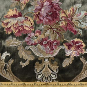 May include: Close-up of a fabric with an embroidered floral design. The flowers are in shades of burgundy, gold, and cream, set against a dark green background. The design includes a decorative vase and ornate leaves. The fabric is likely used for upholstery or drapery.