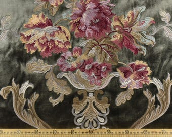 May include: Close-up of a fabric with an embroidered floral design. The flowers are in shades of burgundy, gold, and cream, set against a dark green background. The design includes a decorative vase and ornate leaves. The fabric is likely used for upholstery or drapery.