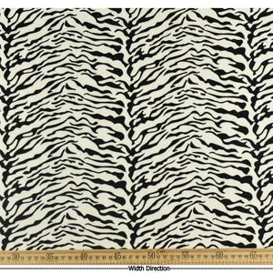 May include: Cream-colored fabric with a black zebra stripe pattern. The fabric has a repeating design of black, irregular stripes on a cream background. A wooden ruler is at the bottom, measuring the width in inches.