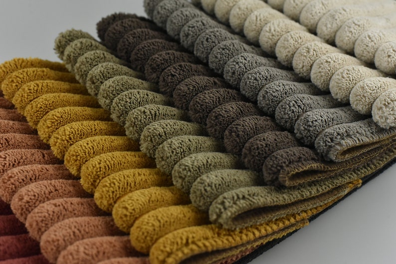 K&ouml;nnte beinhalten: Nahaufnahme eines Stapels Stoffmuster in verschiedenen Braunt&ouml;nen, Gr&uuml;nt&ouml;nen und Beige. Der Stoff hat eine strukturierte, Cord-&auml;hnliche Optik.