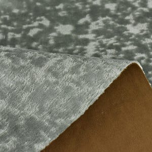 以下が含まれることがあります： 薄い模様のあるグレーの生地のクローズアップ。生地が折り畳まれ、裏地の茶色が現れている。