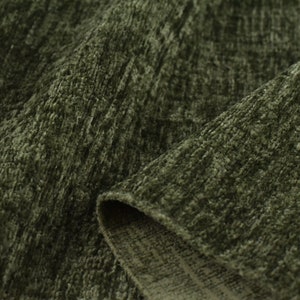 May include: Close-up of a soft, green fabric with a textured, woven pattern. The fabric has a slightly fuzzy appearance and a subtle sheen.