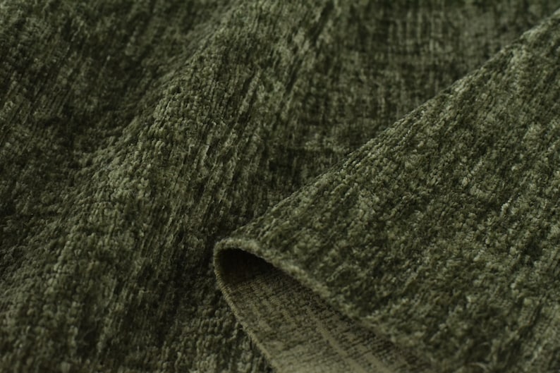 May include: Close-up of a soft, green fabric with a textured, woven pattern. The fabric has a slightly fuzzy appearance and a subtle sheen.
