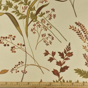 May include: A beige fabric with a repeating pattern of brown and green leaves and flowers. The fabric is measured in inches.