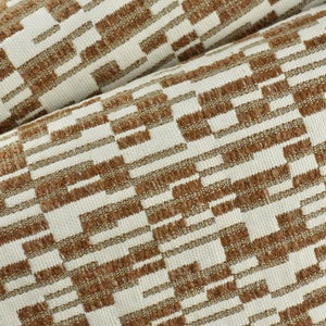 Könnte beinhalten: Nahaufnahme eines braunen und weißen Stoffes mit geometrischem Muster. Der Stoff hat eine strukturierte Oberfläche und einen dezenten Glanz.