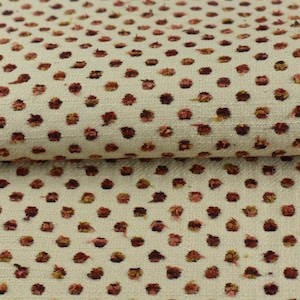 May include: Close-up of a cream-coloured fabric with a repeating pattern of small, red-brown polka dots.