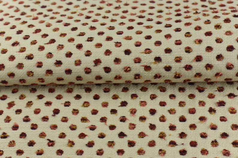 May include: Close-up of a cream-coloured fabric with a repeating pattern of small, red-brown polka dots.