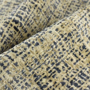 Op de afbeelding: Close-up van een textiel met een herhalend patroon van donkerblauwe en beige vierkanten. De stof is gevouwen en toont diepte en dimensie. Het materiaal heeft een zachte, pluche uitstraling.