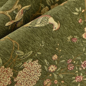 Op de afbeelding: Close-up van groene stof met een bloemen- en vogelpatroon. Het ontwerp toont roze en crèmekleurige bloemen, samen met vogels en takken in een gedetailleerde, getextureerde weefsel. De stof heeft een licht getextureerd uiterlijk.