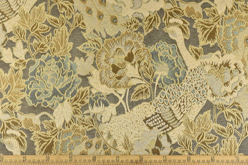K&ouml;nnte beinhalten: Nahaufnahme eines Stoffes mit Blumen- und Vogelmuster. Der Stoff ist eine Tapisserie mit einer strukturierten Oberfl&auml;che. Die Farben sind Gold, Braun und Blau.