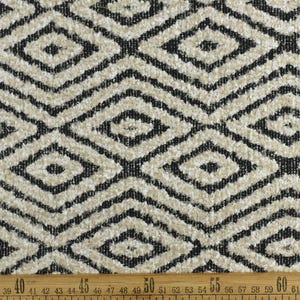 Op de afbeelding: Close-up van een beige en zwarte stof met een geometrisch ruitpatroon. De stof is textuurrijk en heeft een pluche uitstraling.