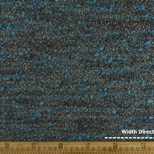 May include: Close-up of a textured fabric with a mix of teal, gray, and gold threads. The fabric has a nubby texture and a subtle sheen. A wooden ruler is at the bottom, showing measurements in inches.