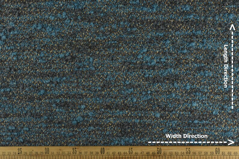 May include: Close-up of a textured fabric with a mix of teal, gray, and gold threads. The fabric has a nubby texture and a subtle sheen. A wooden ruler is at the bottom, showing measurements in inches.