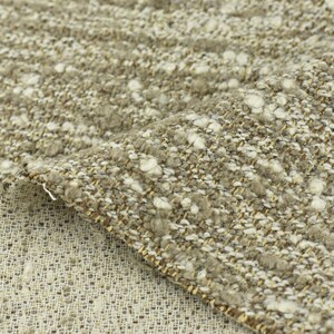 May include: Close-up of a beige and white textured fabric with a subtle sheen. The fabric has a woven appearance with small white flecks throughout.