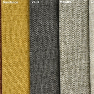 Pode incluir: Cinco amostras de tecido em diferentes cores e texturas. As amostras são etiquetadas como "Peru Tan", "Sundance", "Zeus", "Makara" e "Cloudy".