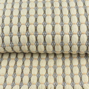 May include: Close-up of a woven fabric with a textured pattern. The fabric is a light beige color with gray and light brown accents.