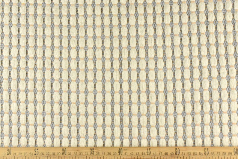 May include: Close-up of a white fabric with a woven pattern of small, light brown circles and thin, gray lines. The fabric is measured with a ruler in inches.