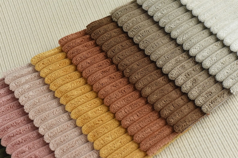 May include: A collection of corduroy fabric swatches in various shades of brown, pink, yellow, and beige. The fabric has a raised, textured pattern.