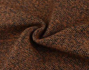 May include: Close-up of a textured fabric with a woven pattern. The fabric is primarily brown with flecks of black and white, creating a mottled appearance. The material is folded, showing depth and texture.