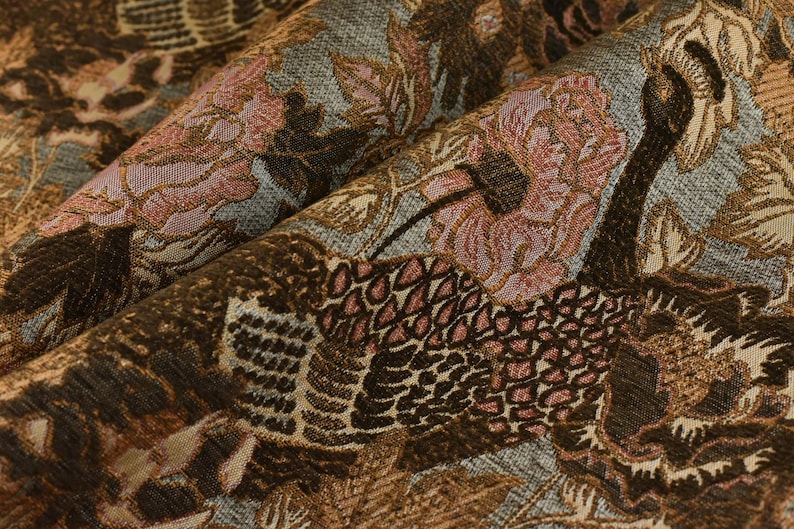 K&ouml;nnte beinhalten: Ein brauner und blauer Stoff mit einem floralen und Vogelmuster. Der Stoff zeigt rosa Blumen, braune V&ouml;gel und ein strukturiertes Design.