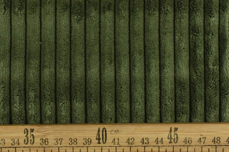 May include: Close-up of a dark green corduroy fabric with a ruler measuring 35 to 45 centimetres.