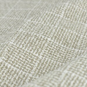 May include: Close-up of a beige fabric with a subtle herringbone pattern. The fabric has a textured, woven appearance.