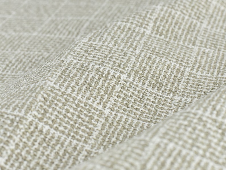 May include: Close-up of a beige fabric with a subtle herringbone pattern. The fabric has a textured, woven appearance.