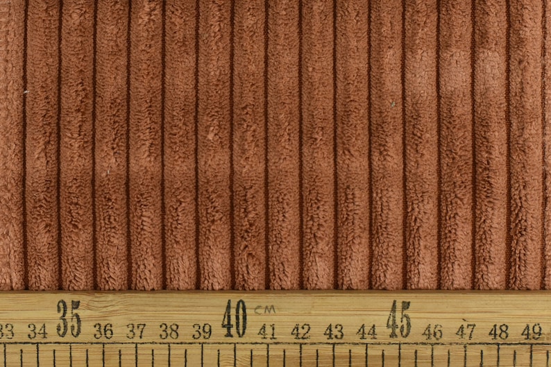 May include: Close-up of a brown corduroy fabric with a ribbed texture. A ruler with markings in centimetres is visible at the bottom of the image. The ruler shows measurements from 33 cm to 49 cm.