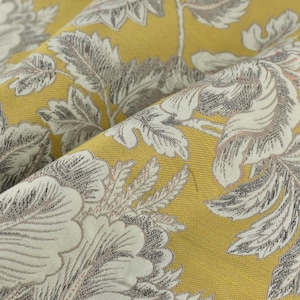 以下が含まれることがあります： 黄色い生地のクローズアップ。花柄のデザインで、グレーと白の大きな花と葉が特徴的で、テクスチャード加工されたレイヤード効果を生み出しています。生地は折りたたまれ、詳細な織り方と色のバリエーションを示しています。