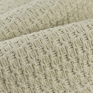 Może przedstawiać: Zbliżenie beżowej tkaniny w splocie waflowym. Tkanina ma fakturowany, tkany wzór.