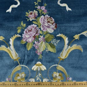 May include: Teal fabric with embroidered floral and scroll design. The design features large purple and pink roses, green leaves, and gold and white scrollwork. A wooden ruler with centimetre measurements is at the bottom of the image.