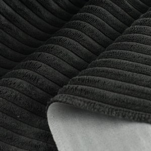 May include: Close-up of black corduroy fabric with a soft, textured surface. The fabric is folded in half, revealing a grey backing.