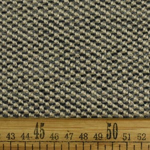 Op de afbeelding: Close-up van een beige en zwarte geweven stof met een diagonaal patroon. Een liniaal met centimetermarkeringen is zichtbaar aan de onderkant van de afbeelding. De liniaal toont metingen van 40 tot 55 centimeter.