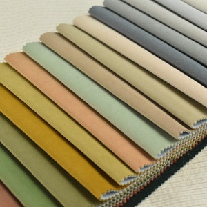 Puede incluir: Una colección de muestras de tela en varios tonos de marrón, verde, beige y gris. Las muestras están dispuestas en forma de abanico, con los tonos más oscuros en la parte inferior y los tonos más claros en la parte superior.