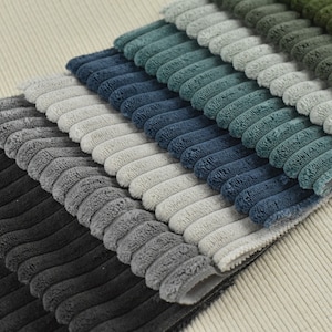 May include: A stack of corduroy fabric swatches in various shades of grey, blue, and green. The fabric has a raised, textured pattern.