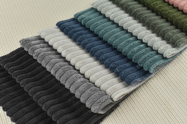 May include: A stack of corduroy fabric swatches in various shades of grey, blue, and green. The fabric has a raised, textured pattern.