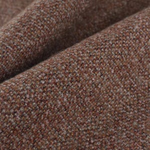 Pode incluir: Close-up de um tecido de tweed marrom com um padrão sutil de espinha de peixe. O tecido tem um toque macio e texturizado.