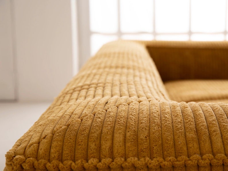 K&ouml;nnte beinhalten: Nahaufnahme eines senfgelben Cord-Sofas mit einer gesteppten Oberfl&auml;che. Das Sofa ist aus einem weichen, pl&uuml;schigen Stoff gefertigt und wirkt komfortabel und einladend.