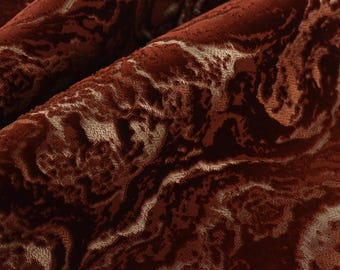 May include: Close-up of a textured fabric with a swirling pattern. The fabric is a deep reddish-brown color with lighter beige accents, creating a marbled effect. The material appears soft and luxurious.