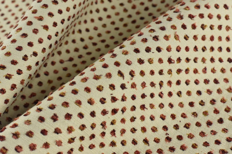 May include: Close-up of a cream-coloured fabric with a repeating pattern of small, dark red dots.