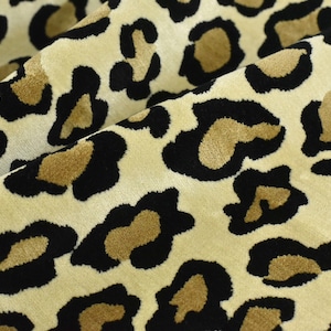 Puede incluir: Tela beige con un estampado de leopardo negro y marrón.