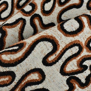 May include: Close-up of a textured fabric with a cream-colored background. The fabric features a repeating pattern of black and brown wavy lines, creating a dynamic and organic design. The fabric is folded, showing its texture.