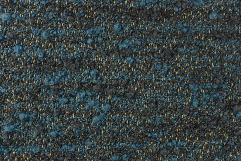May include: Close-up of a textured fabric with a speckled pattern. The fabric features a mix of colors, including teal, dark gray, and gold. The texture appears to be woven, with small, raised areas creating a tactile surface.