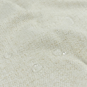 May include: Close-up of a light beige fabric with a textured weave. The fabric is water-resistant and has small water droplets on the surface.