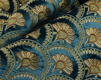 May include: Close-up of teal velvet fabric with an embroidered floral pattern. The design features fan-shaped arrangements of flowers in shades of gold and brown, creating a luxurious and textured appearance. The fabric is folded, showing depth and dimension.
