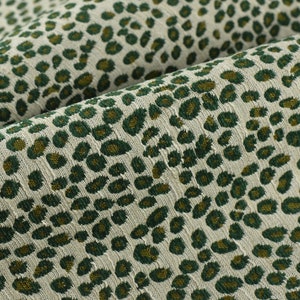 May include: Close-up of a fabric with a green and gold leopard print pattern. The fabric has a textured surface.