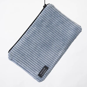 Könnte beinhalten: Eine hellblaue Cord-Zipper-Tasche mit einem schwarzen Reißverschluss und einem schwarzen Etikett mit der Aufschrift "MALAKA manufacturer".