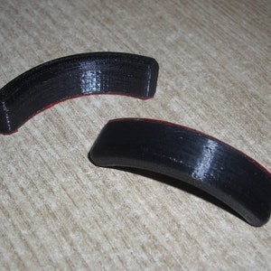 Puede incluir: Dos piezas curvas de plástico negro con un borde rojo. Las piezas son similares en forma y tamaño.