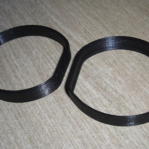 Puede incluir: Dos anillos de plástico negro, posiblemente para un proyecto artesanal o para sujetar algo.